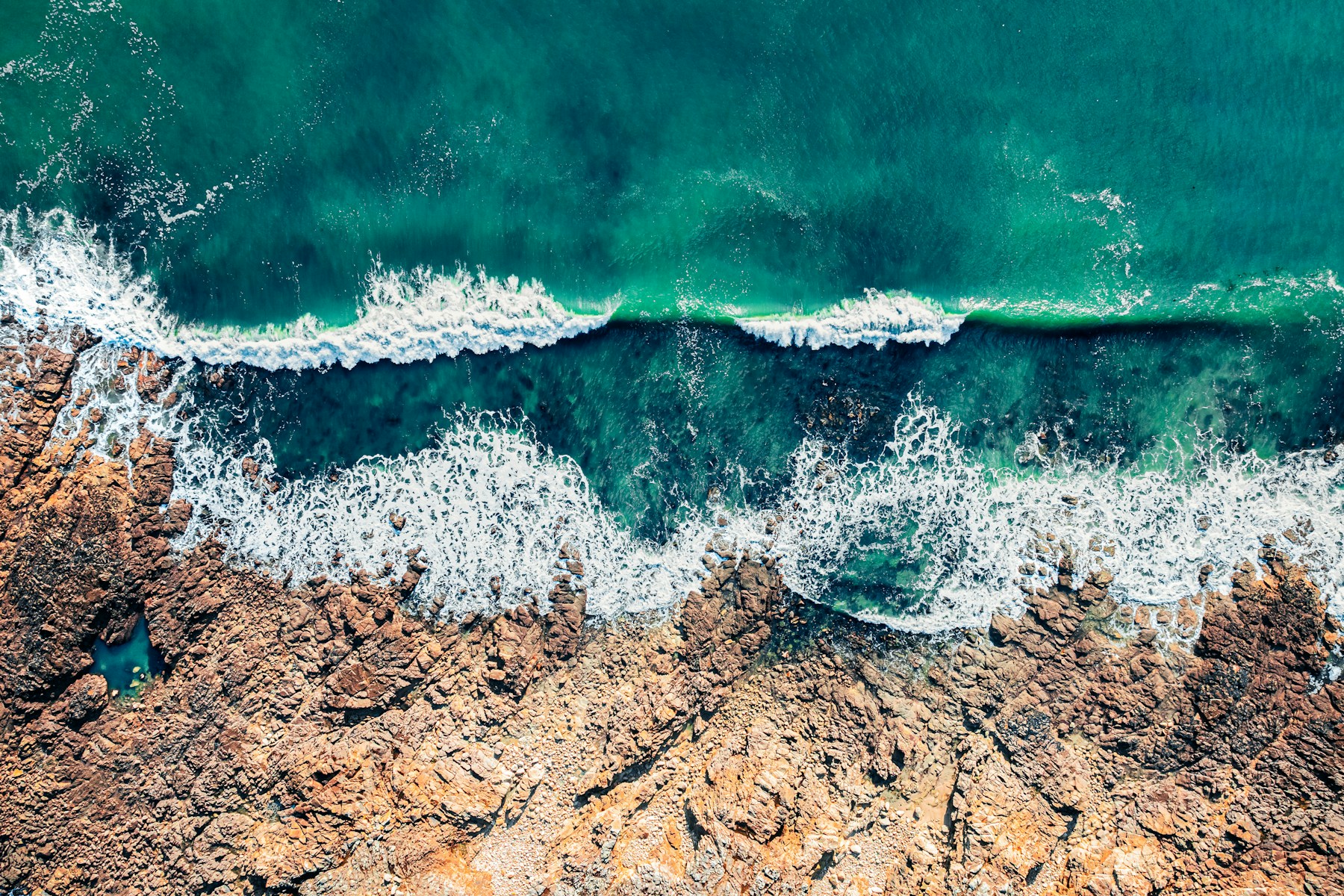 Blue ocean waves meeting an orange-brown rocky shore
